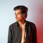 Young man in a studio wearing headphones with a colorful backdrop.